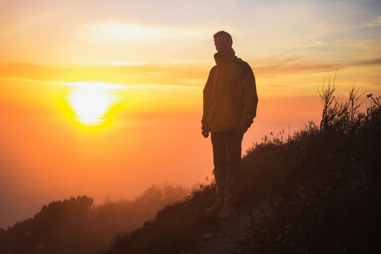 man in white jacket standing on mountain during sunset